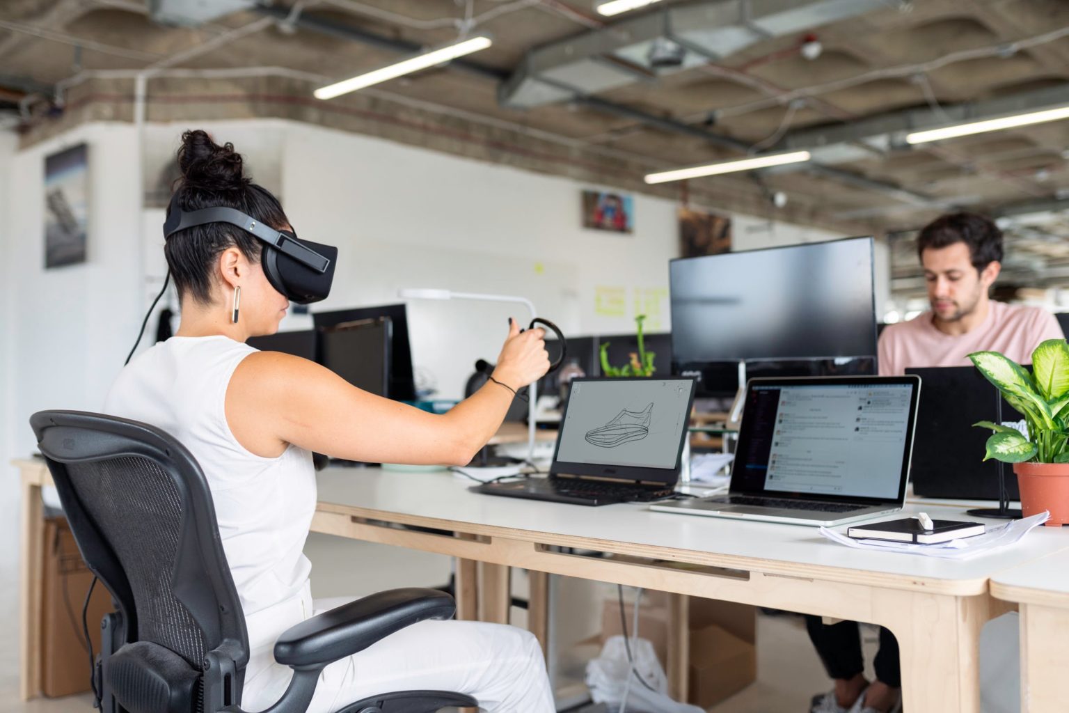 a woman wearing headphones sitting at a desk with a laptop and a man sitting at the computer