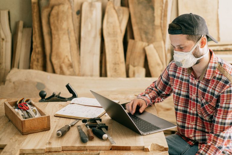 a person with a white mask on the face sitting at a table with a laptop and papers and