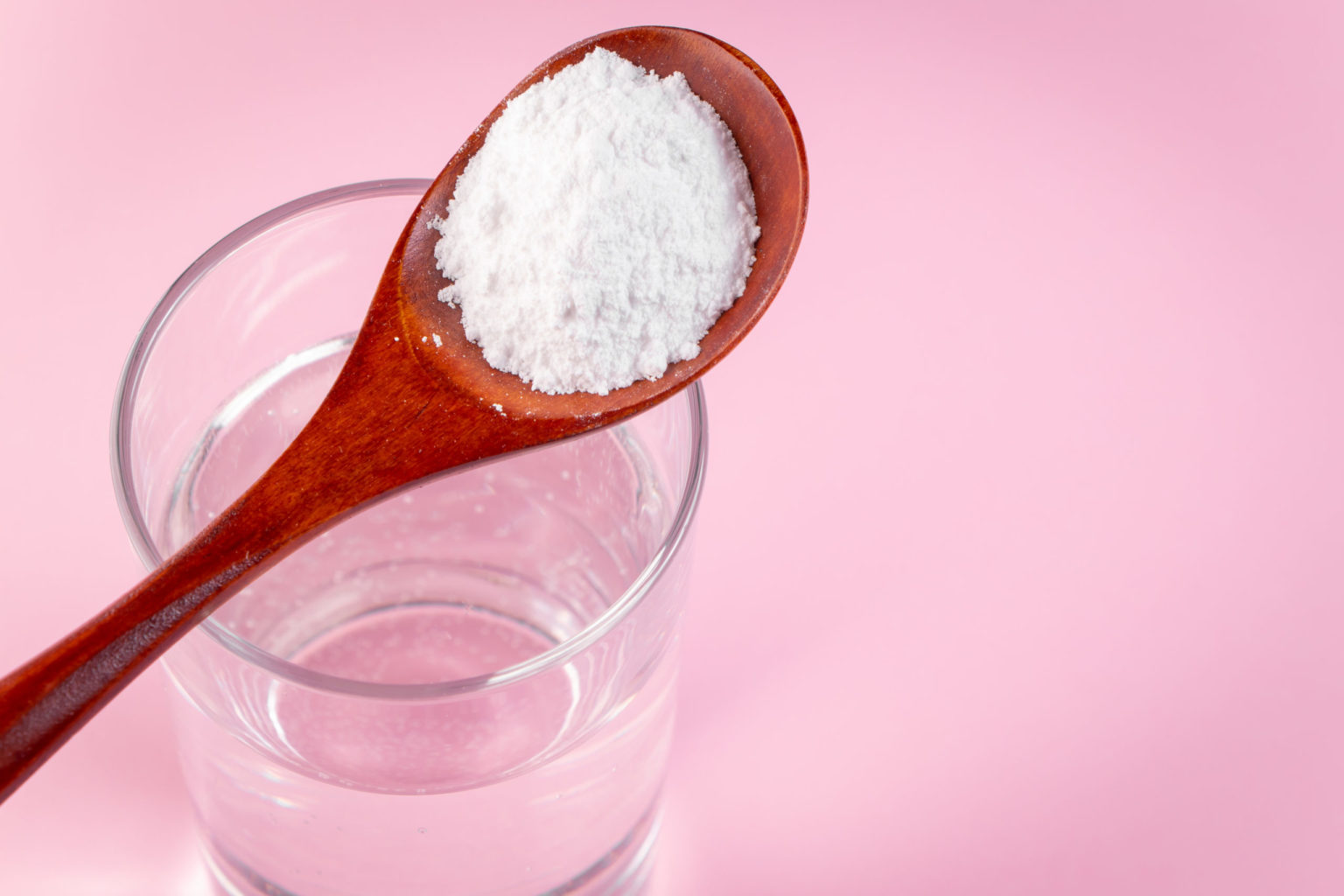 Natural bio supplement collagen powder in wooden spoon and glass of pure water on pink background.