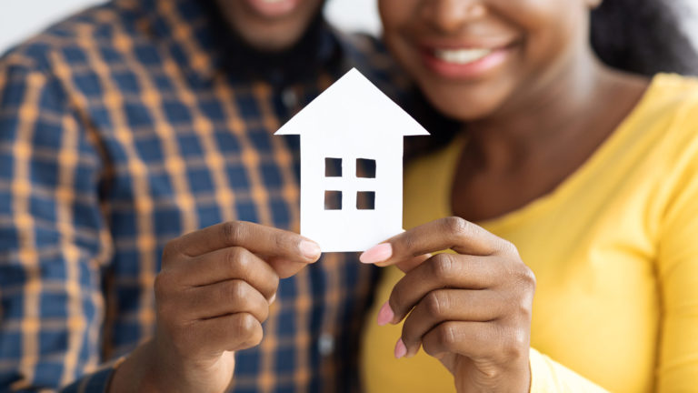 New Home Owners. Happy african american spouses holding paper house figure