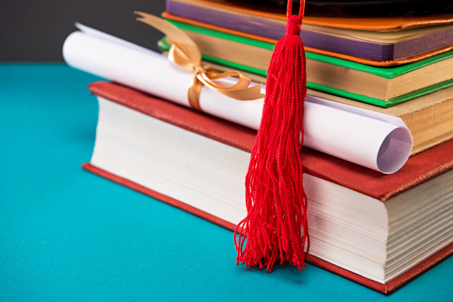 close up of books, diploma and graduation cap with tassel on blue, education concept